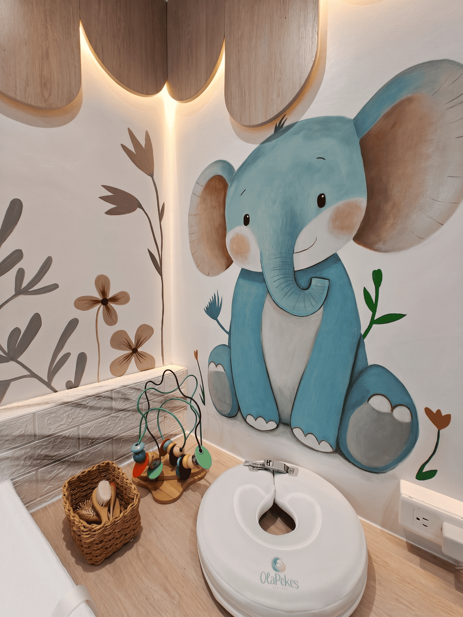 Decoración interior de Ola Pekes en Cuenca: mural de elefante tierno, flotador de cuello de spa para bebés y juguetes de madera sobre encimera.